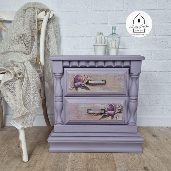 A vintage 2-drawer nightstand refurbished by Stacey Jordan Furniture features Dixie Belle's Morning Sunrise Silk All-In-One Mineral Paint and purple flower details on the drawers.
