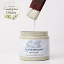 Jar of Silk all-in-one mineral paint with a brush dripping paint onto it, against a white background.