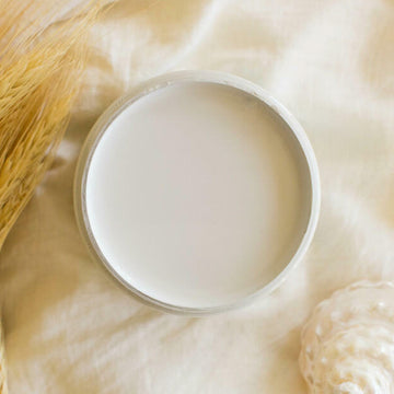 An arial view of an open container of Dixie Belle Paint Company's Oyster All-In-One Silk Paint is on a white material with dried golden wheat sprigs.