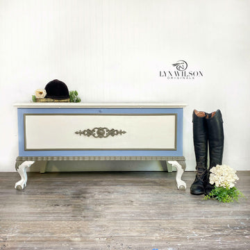 A vintage storage bench refurbished by Lyn Wilson Originals has silver and white details and features Dixie Belle's Quiet Cove Silk All-In-One Mineral Paint.