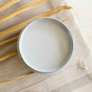 An arial view of an open container of Dixie Belle Paint Company's Quiet Cove All-In-One Silk Paint is on a white material with dried palm frond.