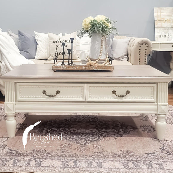 A vintage coffee table with drawers refurbished by Brushed by Maddie features Dixie Belle's Sand Castle Silk All-In-One Mineral Paint.