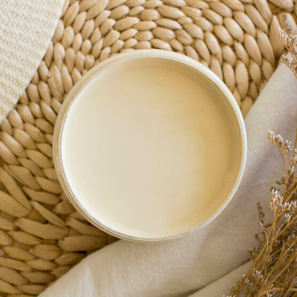 An arial view of an open container of Dixie Belle Paint Company's Sand Castle All-In-One Silk Paint is on a weaved wicker placemat with white cloth napkins and dried beach flowers.