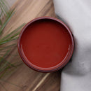 An arial view of an open container of Dixie Belle Paint Company's Sequoia All-In-One Silk Paint is on a wood table with a white cloth napkin and green grassy foliage.
