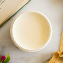 An arial view of an open container of Dixie Belle Paint Company's Sun Kissed All-In-One Silk Paint is on a white table with an open book and yellow material.