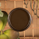 An arial view of an open container of Dixie Belle Paint Company's Umber All-In-One Silk Paint is on a copper rack over a sand brown table with succulents.