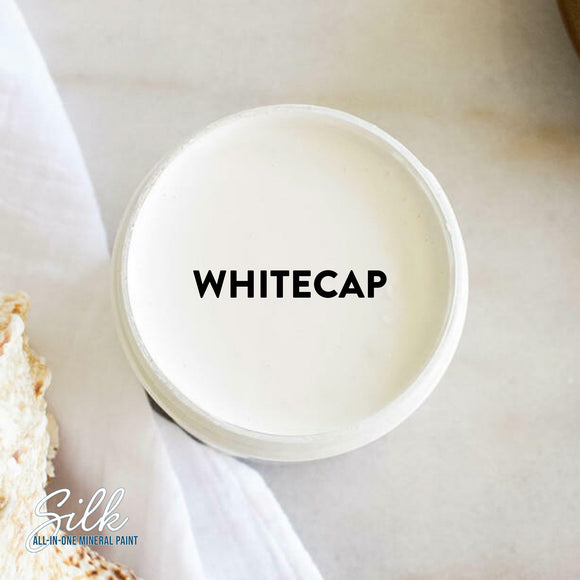 An arial view of an open container of Dixie Belle Paint Company's Whitecap Silk All-In-One Mineral Paint is shown with black text reading Whitecap.