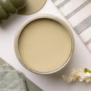 An arial view of an open container of Dixie Belle Paint Company's Olive Wood Chalk Mineral Paint is on a white table with other items.