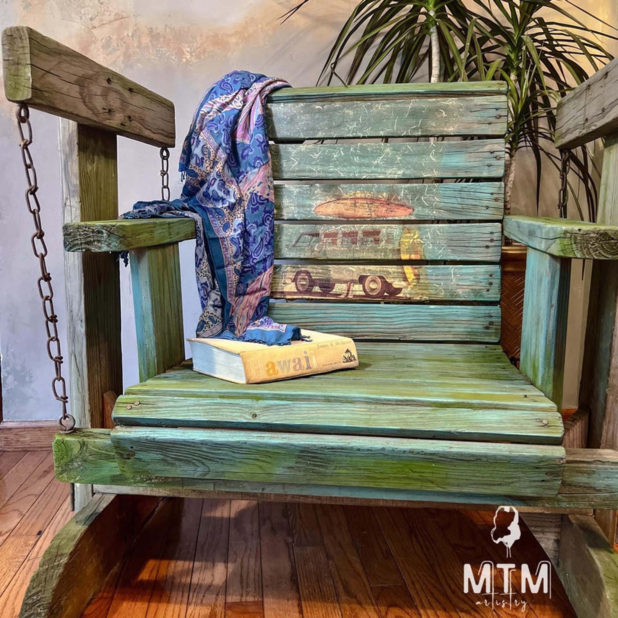 A vintage wood porch glider chair refurbished by MTM Artistry is stained green and beachy blue and features Belles and Whistles' Surf's Up A1 rice paper on the chair back.