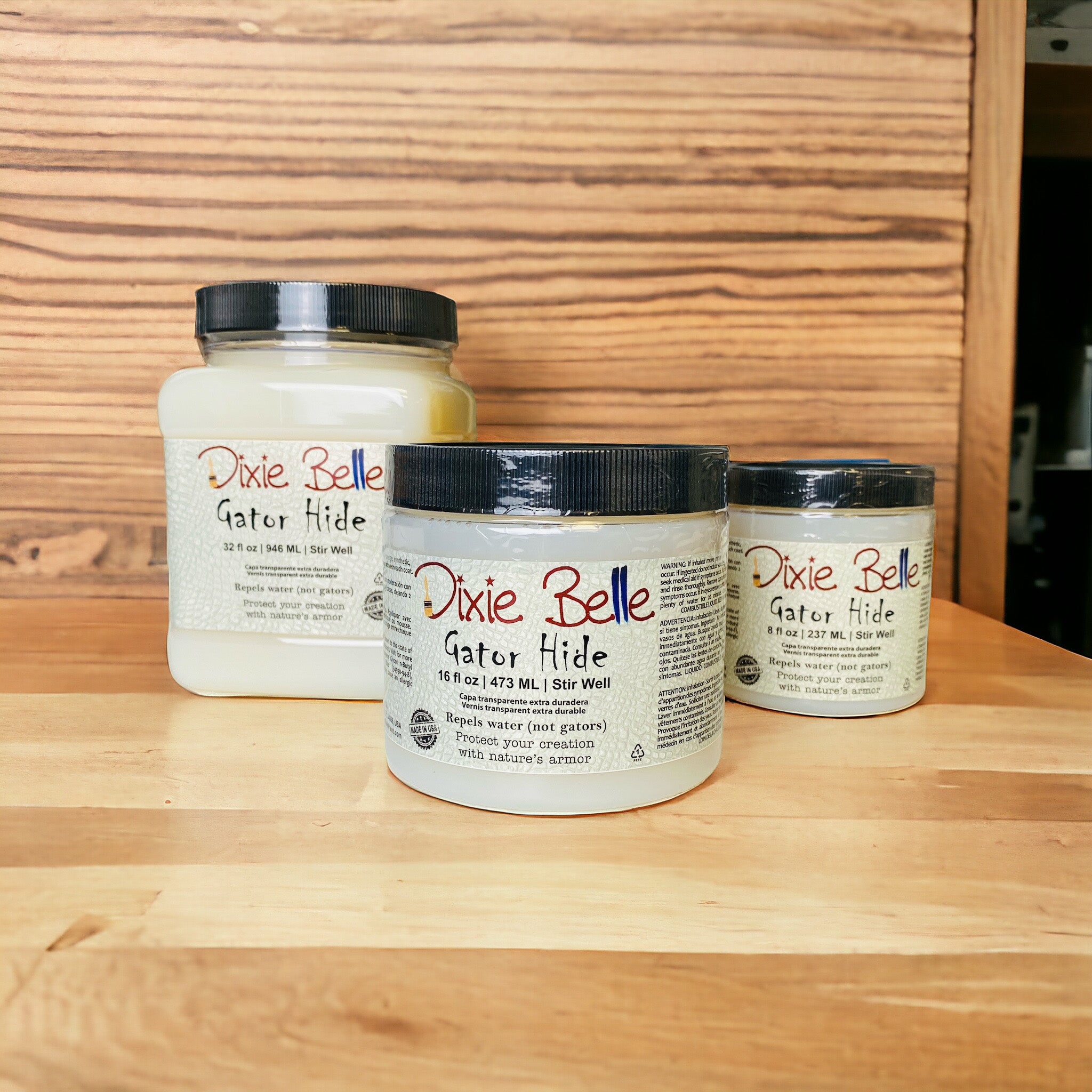 Three containers of Dixie Belle Paint Company's Gator Hide in 3 sizes (32, 16, and 8 fluid ounces) are against a wood background.