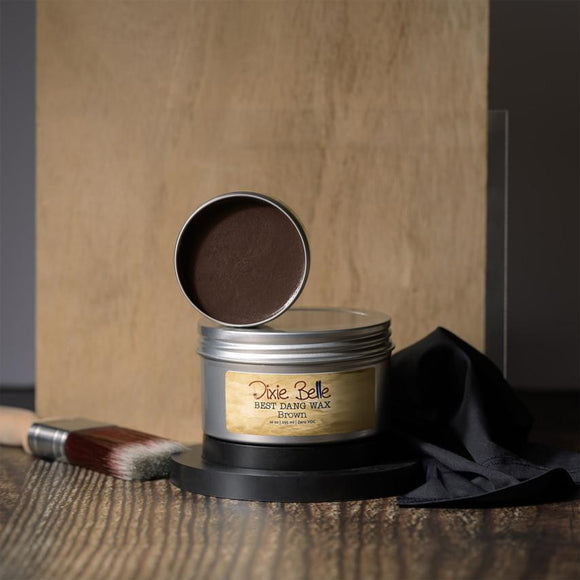 Metallic container of Dixie Belle wood wax with a brush and black cloth on a wooden surface.