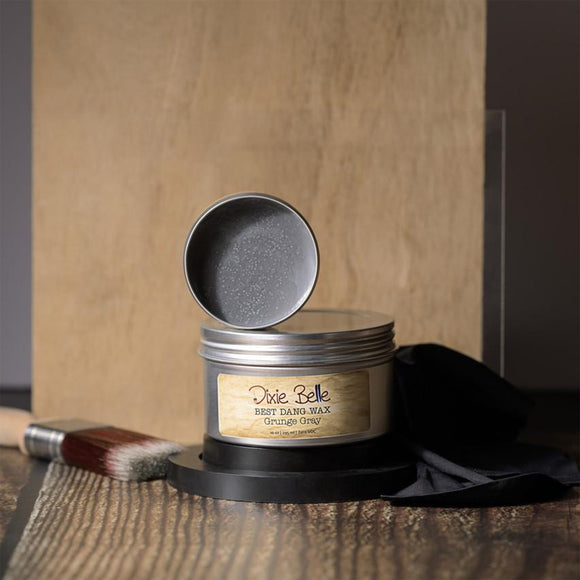 Metallic wax container with open lid on a wooden surface, featuring 'Dixie Belle' branding.