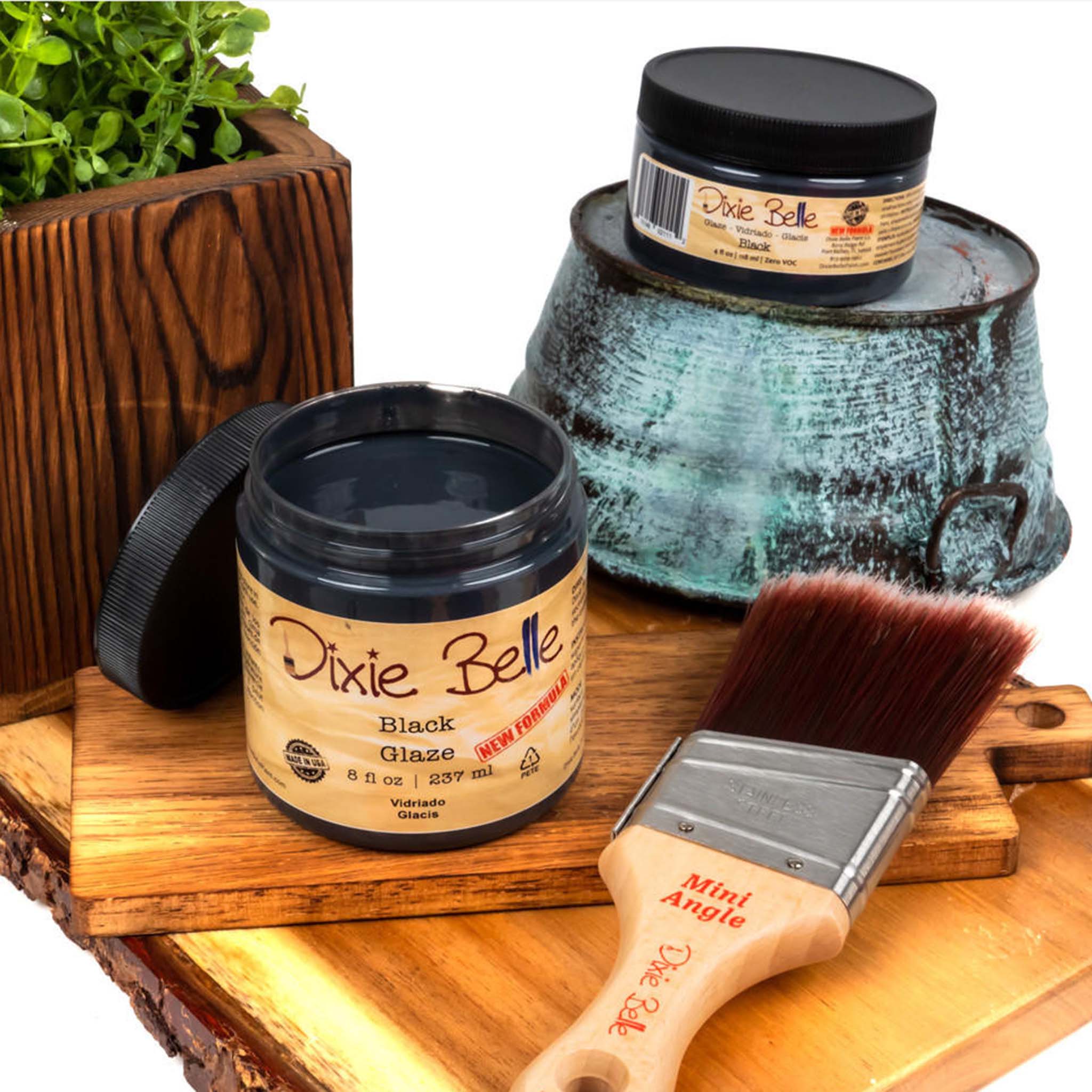 An 8oz/237ml and 4oz/118ml of Dixie Belle Paint's Black Glaze are featured on a wood shelf with a Dixie Belle mini Angle paint brush. 