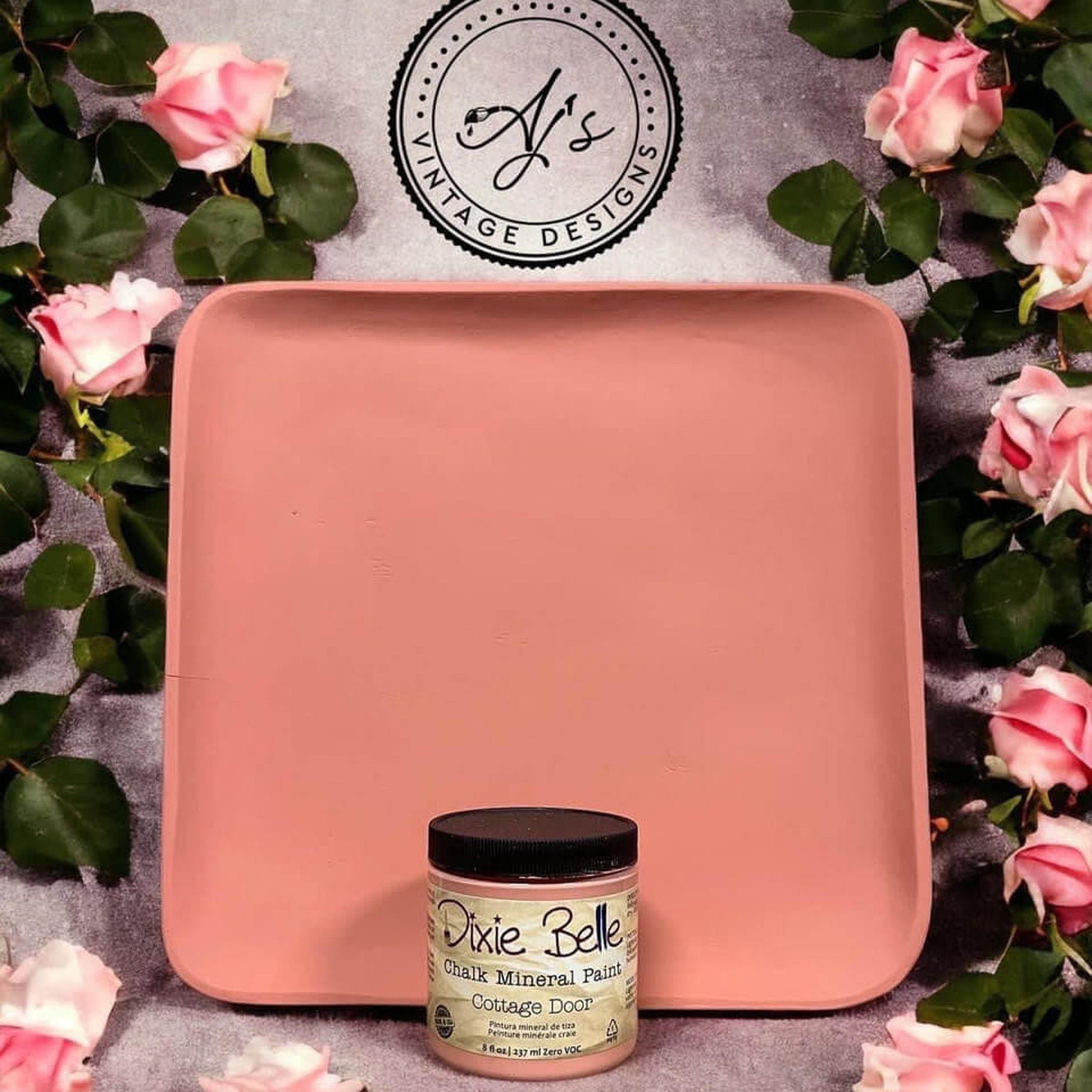 A wood tray repainted by AJ's Vintage Designs using Dixie Belle's Cottage Door chalk mineral paint is pictured with a container of the paint. Pink roses with green foliage surround the tray.