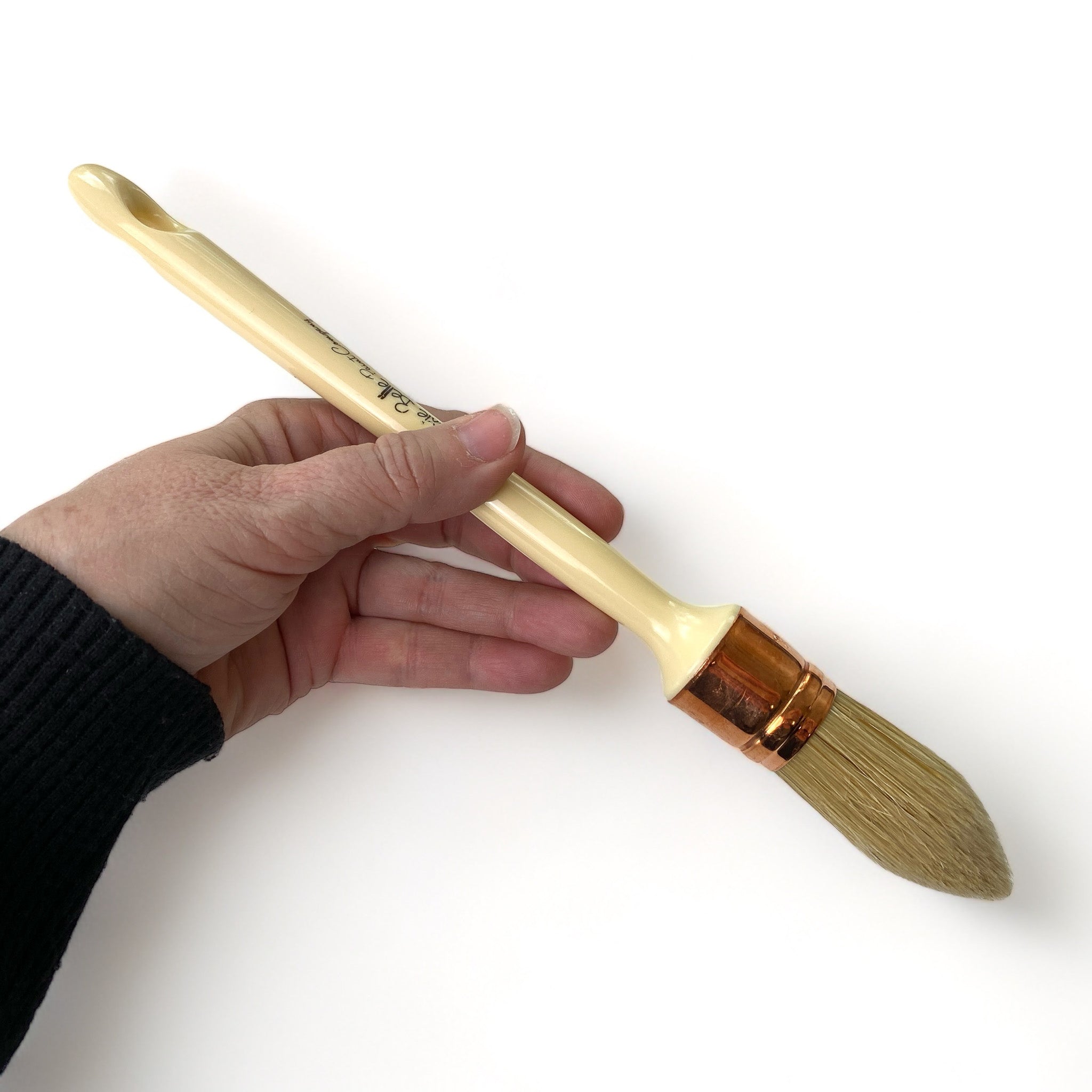 A hand is shown holding Dixie Belle's French Tip Paint Brush is against a white background. This brush has natural bristles and is shaped to help reach the fine-detailed areas on your furniture projects.