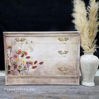 A 3-drawer dresser defurbished by Jodie Flavell Art is painted a blend of beige and white and features the Pink Pampas and Dried Wilds on its drawers.