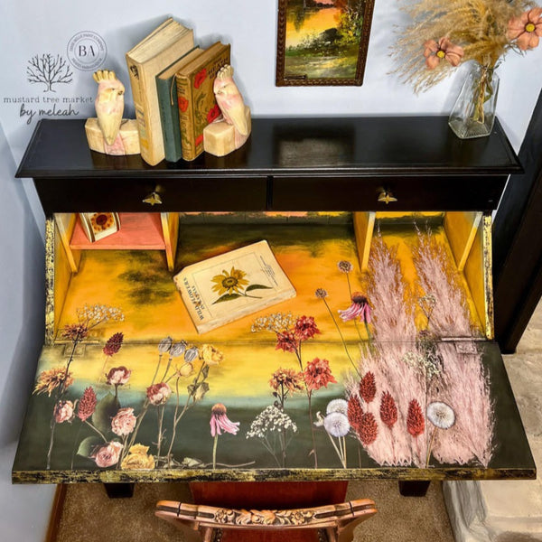 A vintage secretary's desk refurbished by Mustard Tree Market by Meleah is painted black and features the Pink Pampas and Dried Wilds against a yellow and dark green background inside its drop-down door.