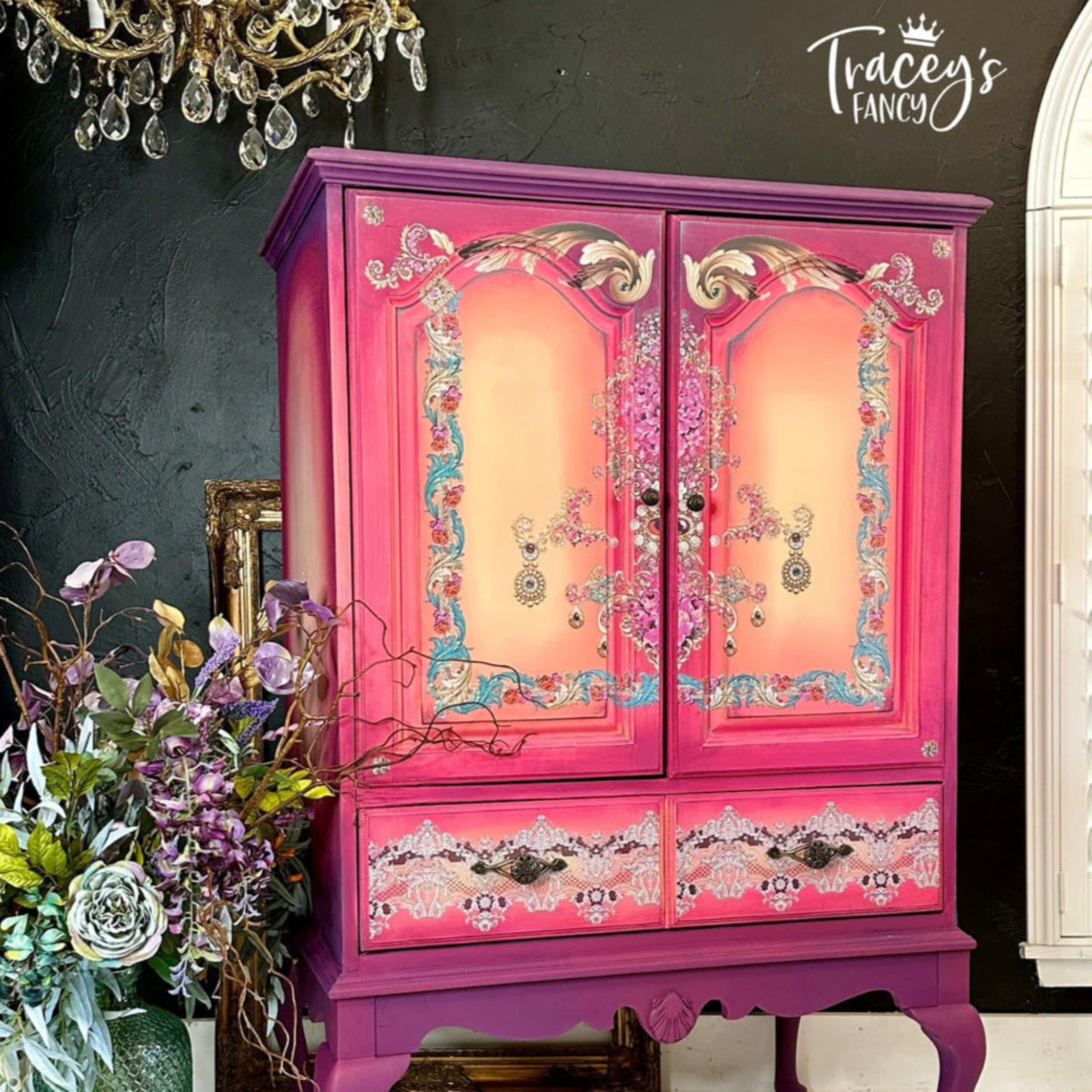 A vintage armoire refurbished by Tracy's Fancy is painted a blend of purples, pinks, and yellow and features Belles & Whistles The Gilded Age transfer on it.