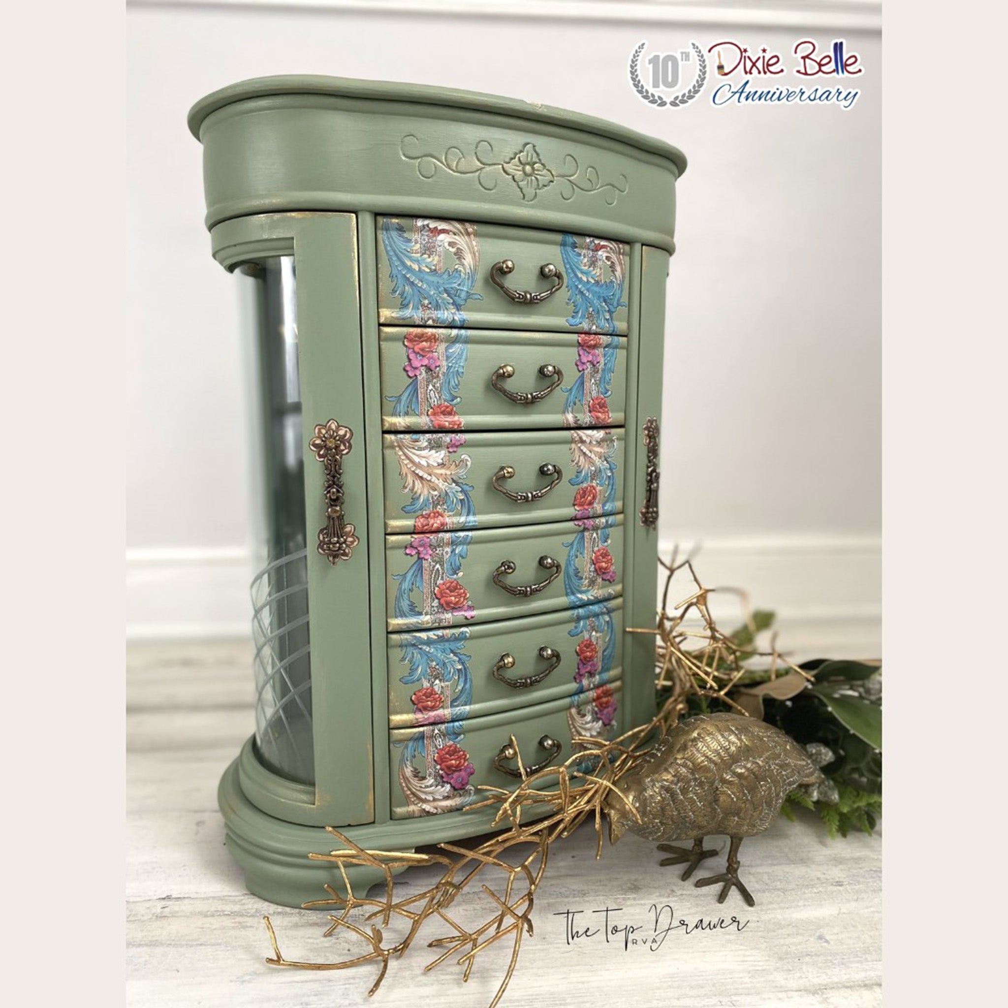 A vintage tabletop jewelry armoire refurbished by The Top Drawer is painted sage green and features ReDesign with Prima's The Gilded Age transfer on its 6 small drawers.