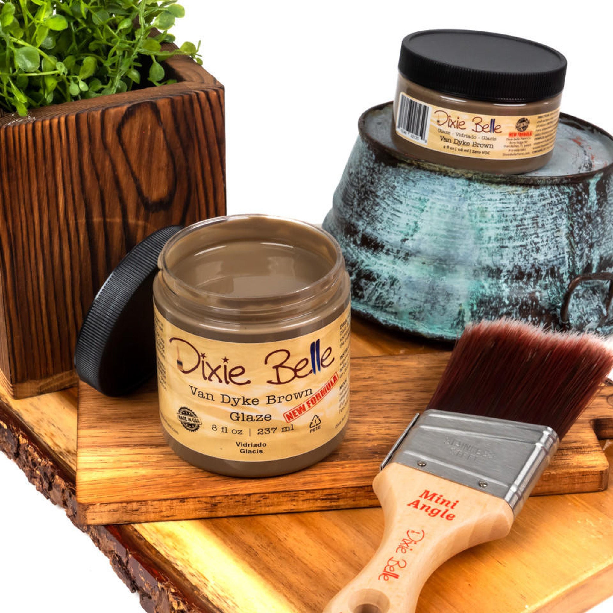 An 8oz/237ml and 4oz/118ml of Dixie Belle Paint's Van Dyke Brown Glaze are featured on a wood shelf with a Dixie Belle mini Angle paint brush.