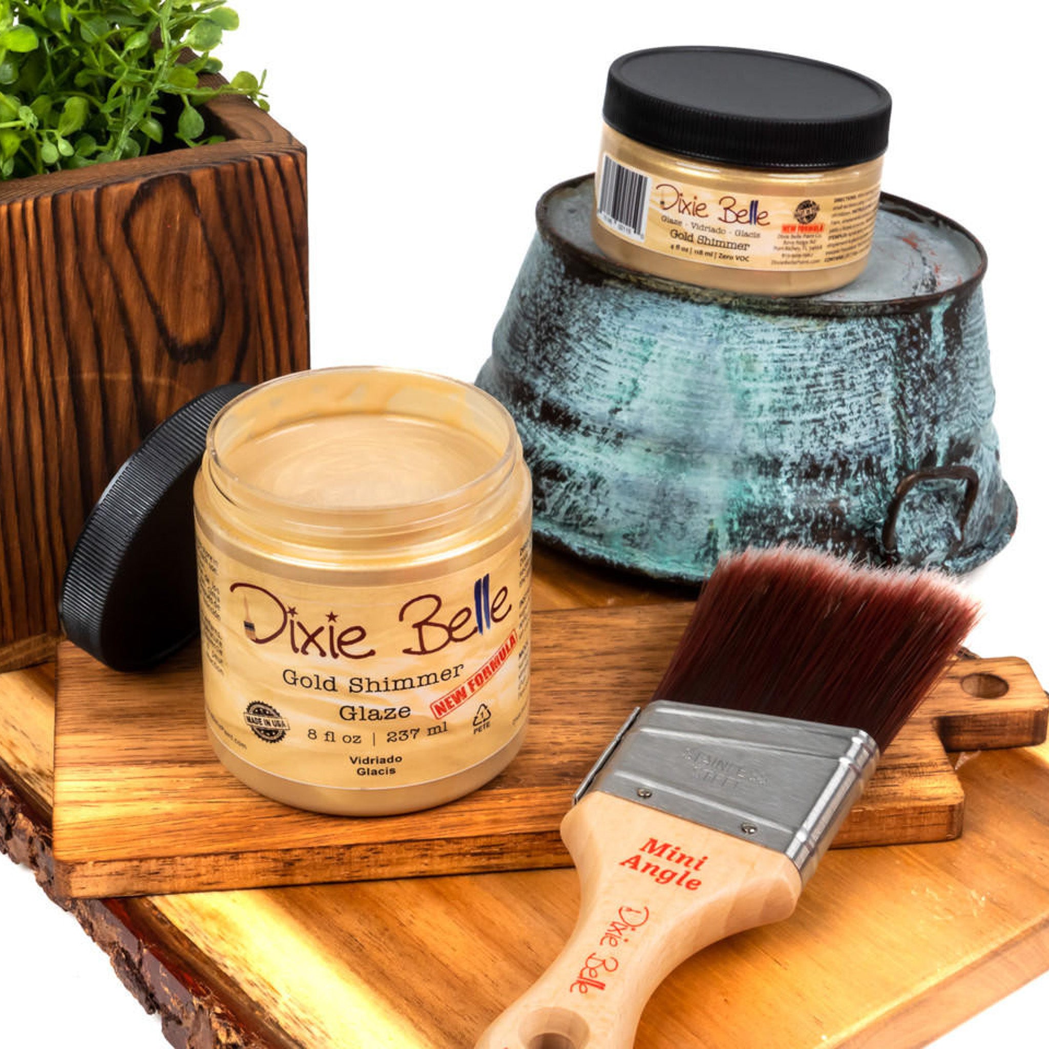 An 8oz/237ml and 4oz/118ml of Dixie Belle Paint's Gold Shimmer Glaze are featured on a wood shelf with a Dixie Belle mini Angle paint brush.