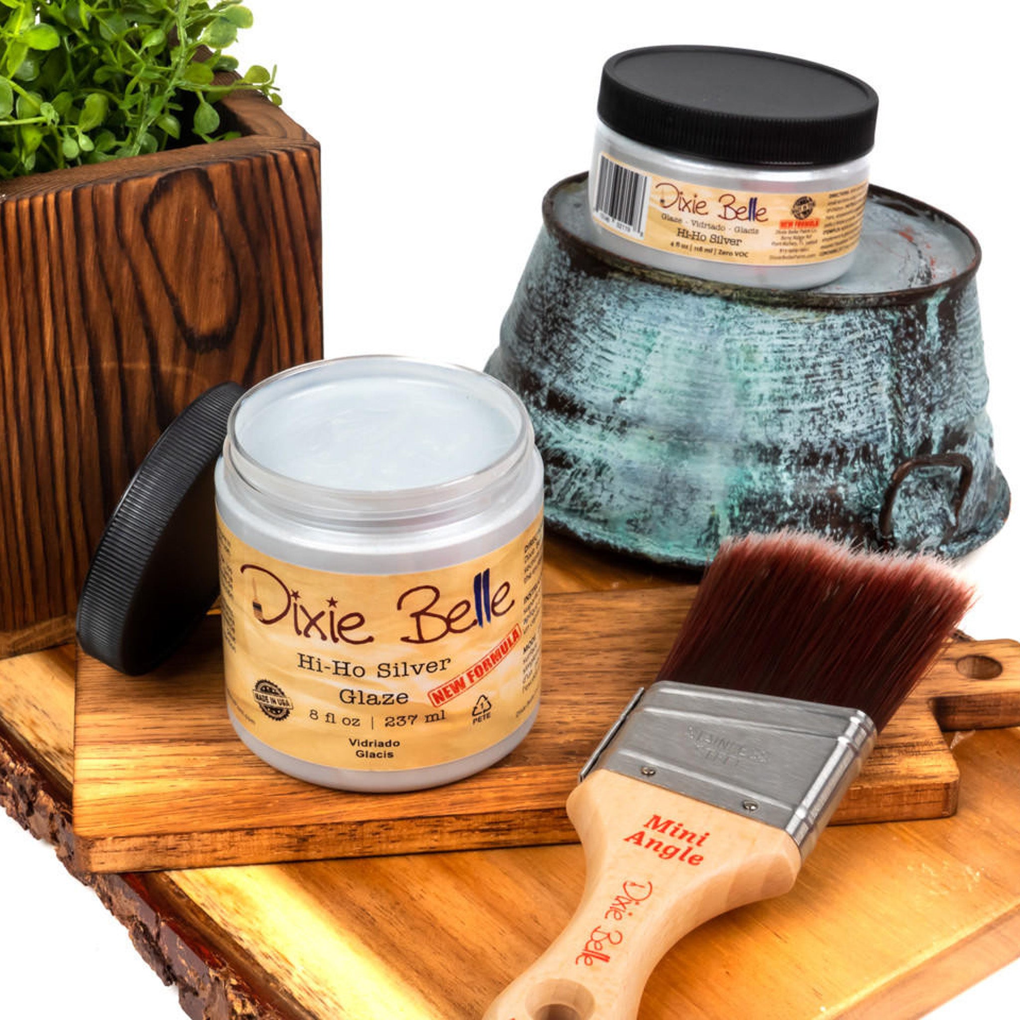 An 8oz/237ml and 4oz/118ml of Dixie Belle Paint's Hi Ho Silver Glaze are featured on a wood shelf with a Dixie Belle mini Angle paint brush.
