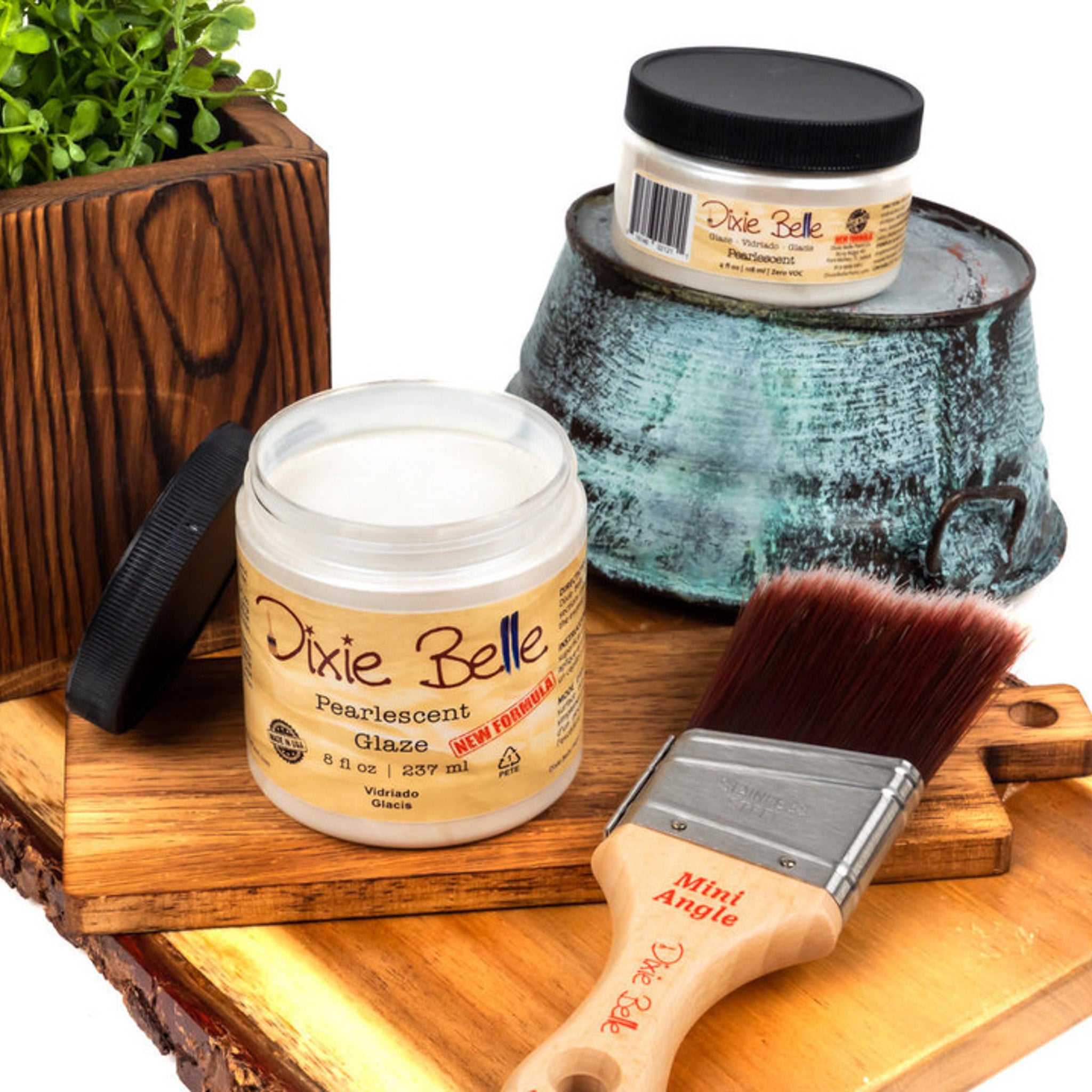 An 8oz/237ml and 4oz/118ml of Dixie Belle Paint's Pearlescent Glaze are featured on a wood shelf with a Dixie Belle mini Angle paint brush.