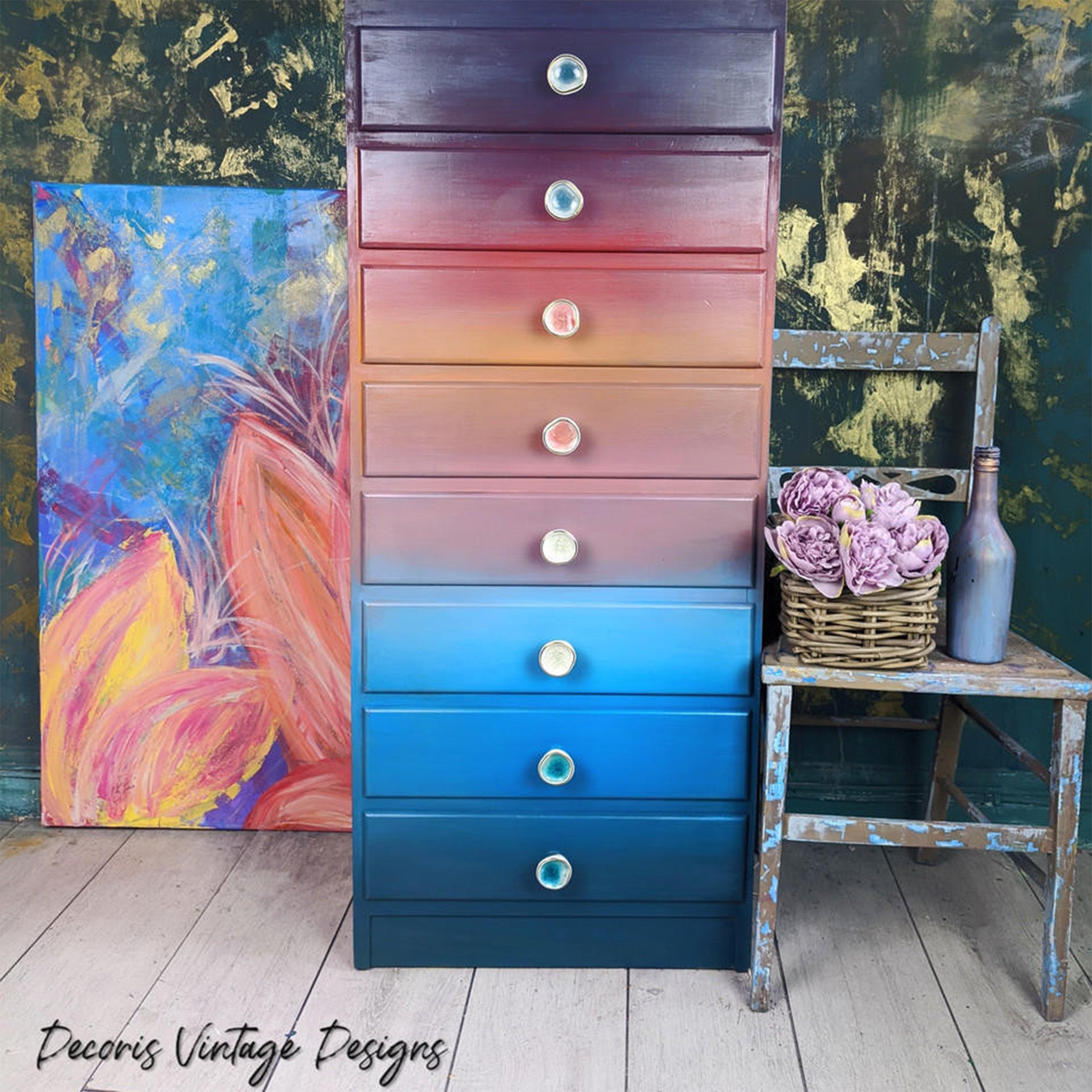 An 8-drawer chest dresser refurbished by Decoris Vintage Designs is painted and ombre of purple, red, orange, light blue and dark blue and features Dixie Belle Paint's Pearlescent Glaze on it.