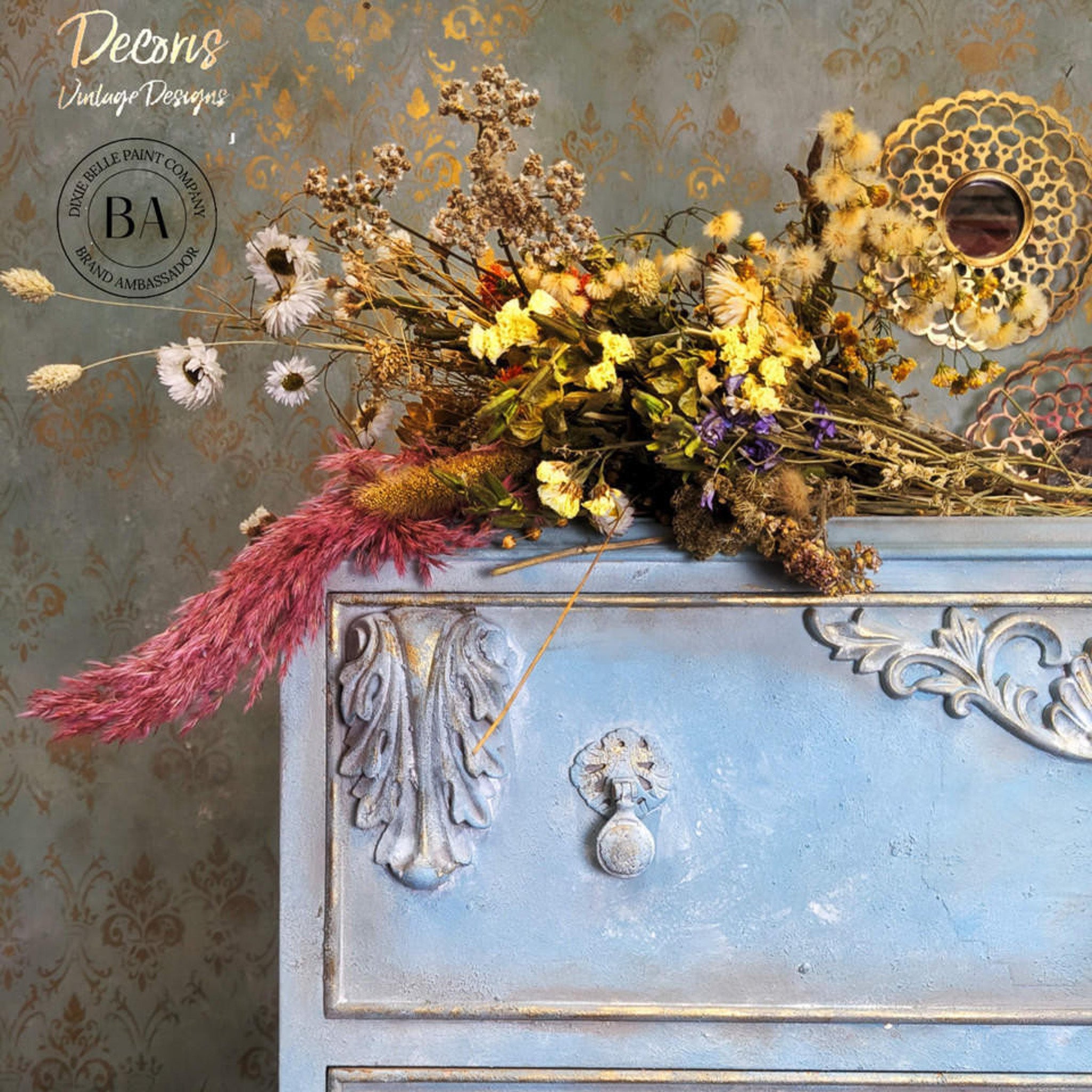 A close-up of a vintage dresser refurbished by Decoris Vintage Designs is painted light blue with gold accents and features Dixie Belle Paint's Whitewash Glaze to accent detailed areas.