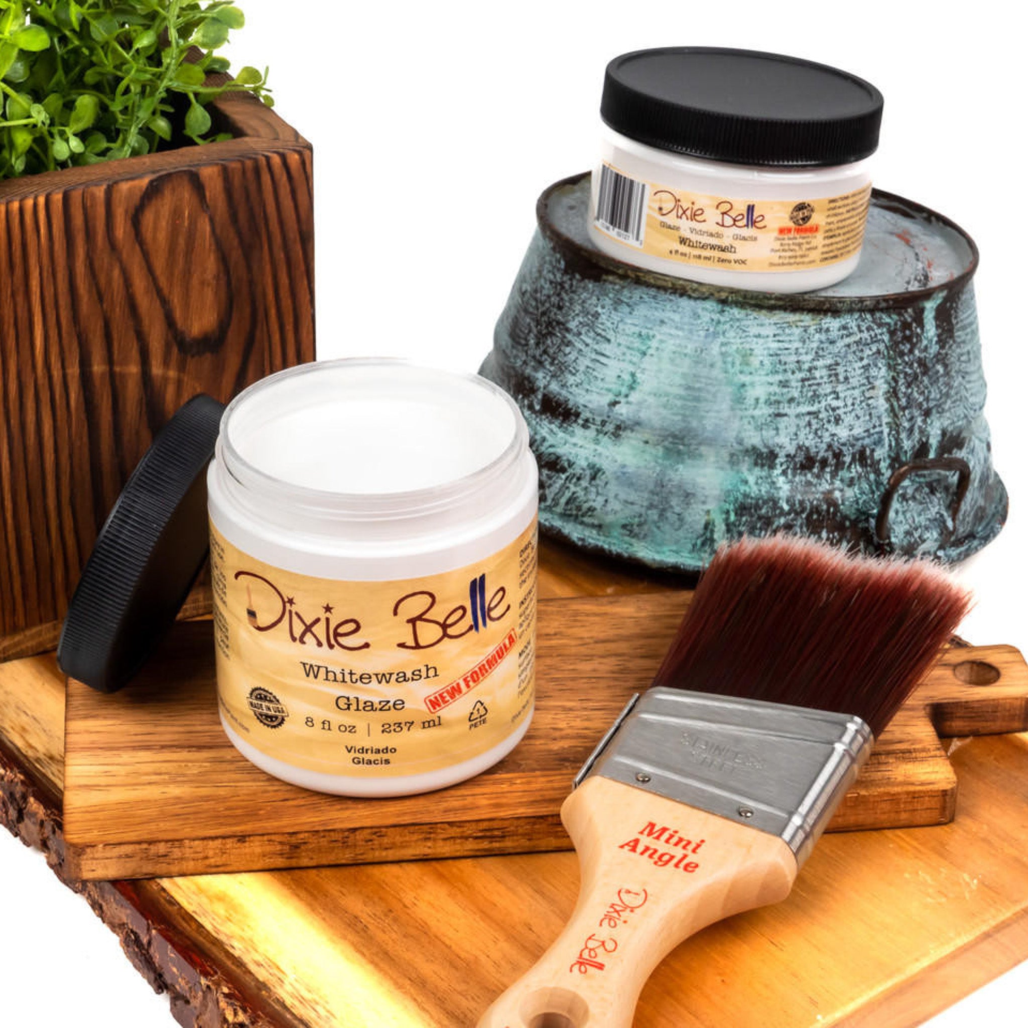 An 8oz/237ml and 4oz/118ml of Dixie Belle Paint's Whitewash Glaze are featured on a wood shelf with a Dixie Belle mini Angle paint brush.
