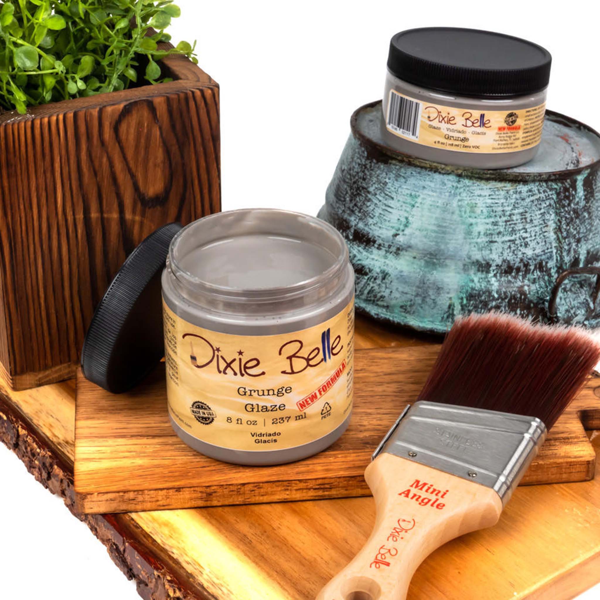 An 8oz/237ml and 4oz/118ml of Dixie Belle Paint's Grunge Glaze are featured on a wood shelf with a Dixie Belle mini Angle paint brush.