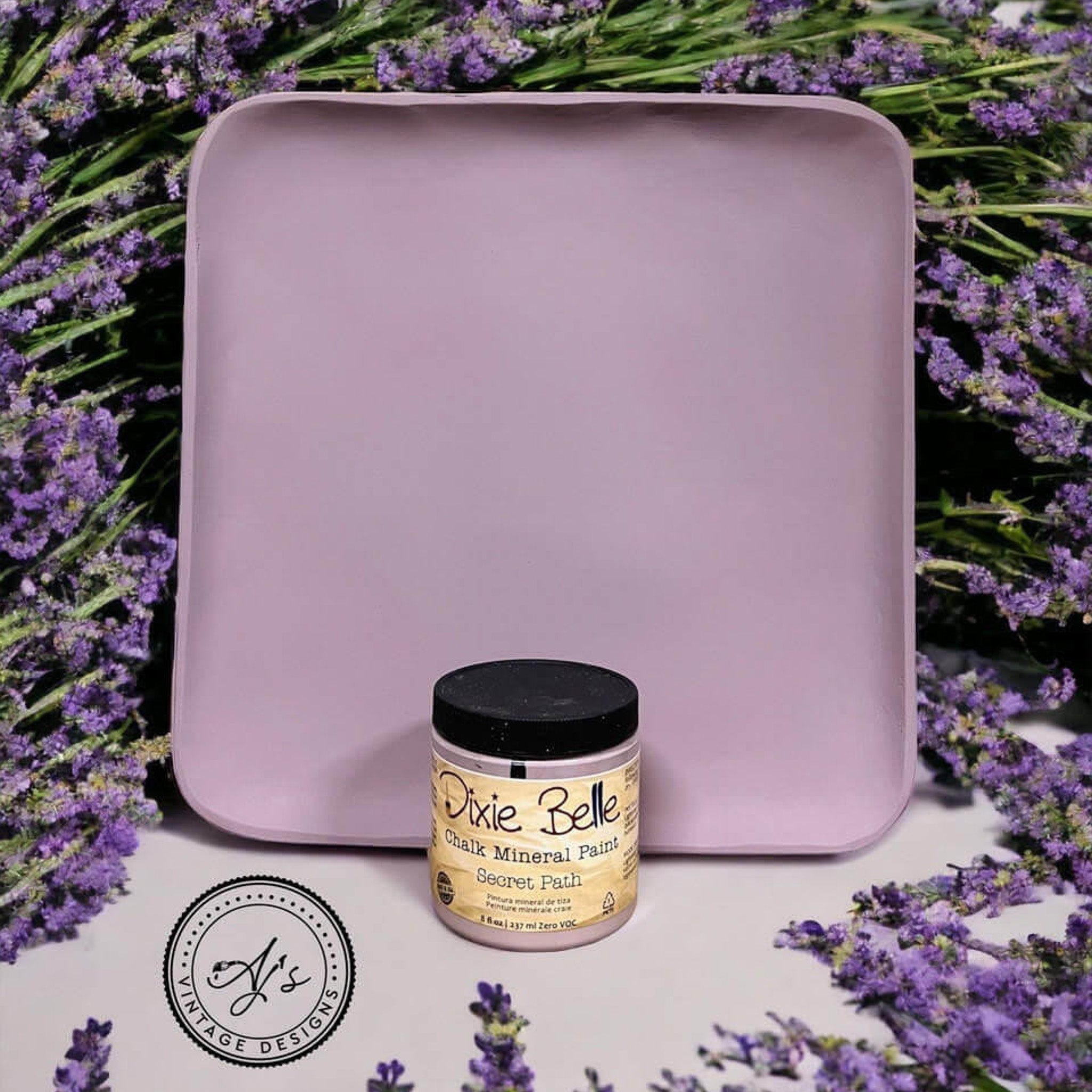 A square wood tray refurbished by Aj's Vintage Design is painted in Dixie Belle's Secret Path chalk mineral paint. The tray is surrounded by lavender flowers and the container of paint sits in front of the tray.