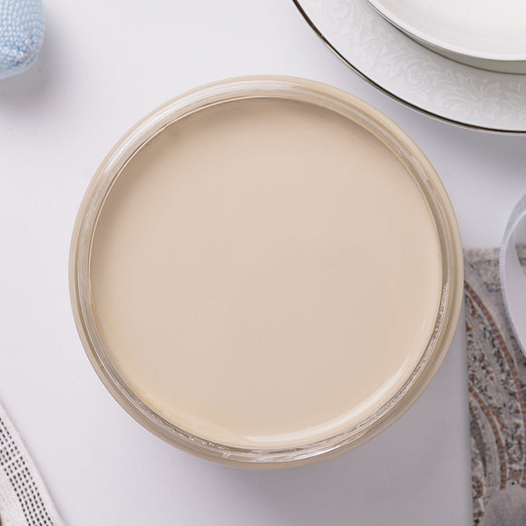 Jar of cream paint on a white surface with a mirror and towel in the background