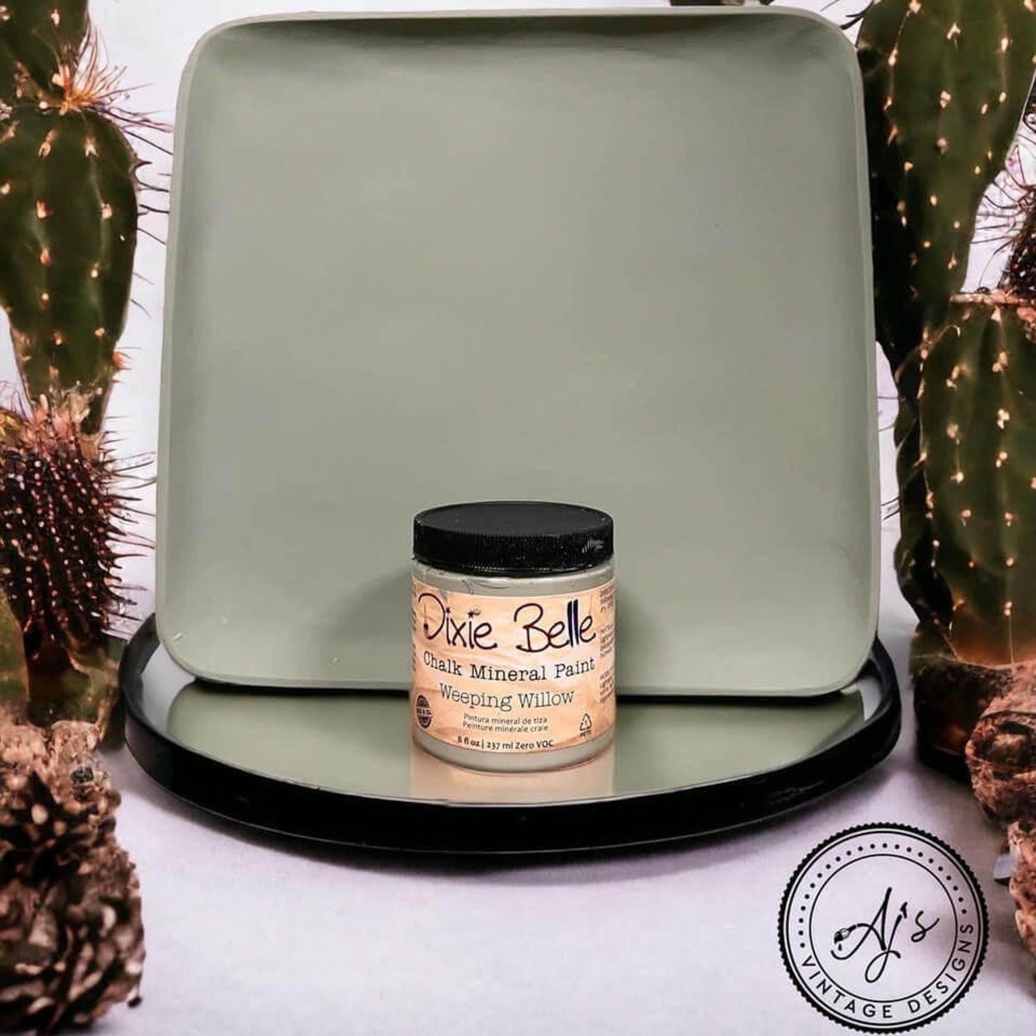 A square wood tray refurbished by Aj's Vintage Designs  is painted in Dixie Belle's Weeping Willow chalk mineral paint. The tray is sat up on end with a container of Dixie Belle's Weeping Willow chalk mineral paint in front of it and they are surrounded by catus.
