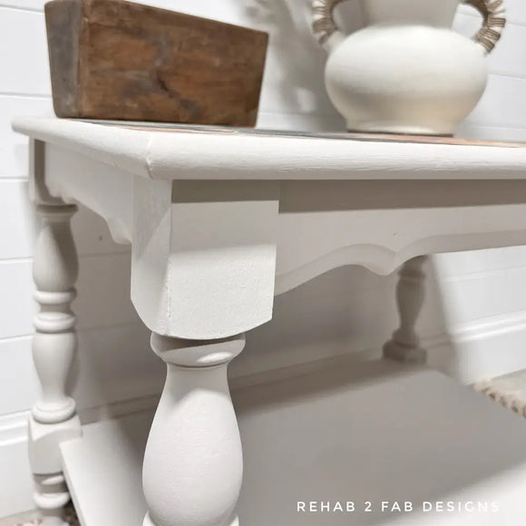 White wooden table with decorative items against a white wall, featuring 'Rehab 2 Fab Designs' branding.