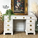 White desk with gold accents in a room with decorative elements like a painting and plants.