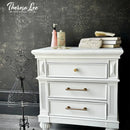 White dresser with decorative items against a dark wall with floral patterns, featuring the brand 'Theresa Lee'.
