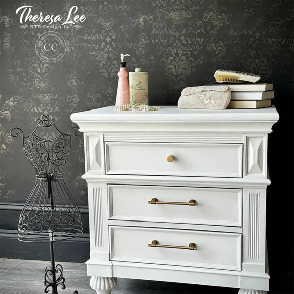 White dresser with decorative items against a dark wall with floral patterns, featuring the brand 'Theresa Lee'.