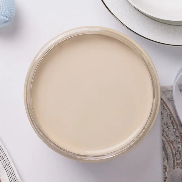 Jar of cream paint on a white surface with a mirror and towel in the background