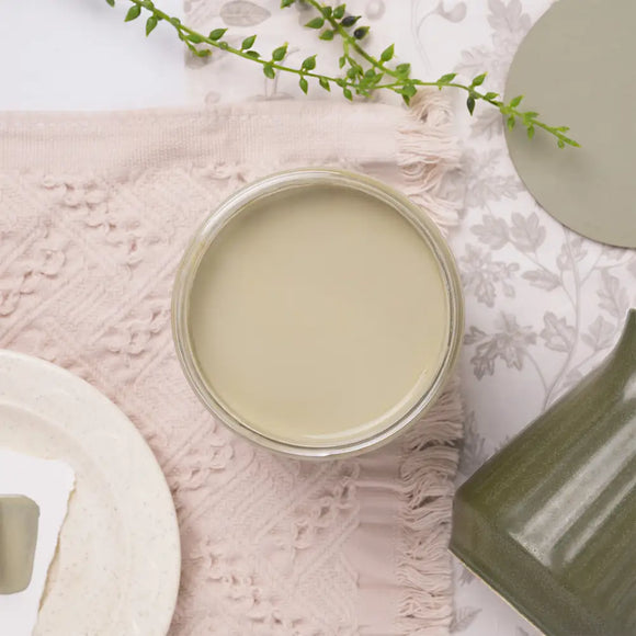 Jar of light-colored green paint on a textured surface with decorative elements