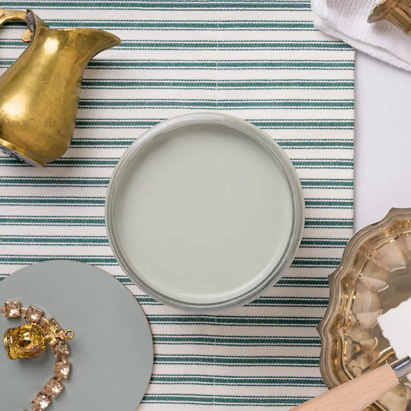 Jar of light green paint on  striped tablecloth with decorative objects