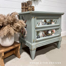 Gray nightstand with decorative elements on a light wooden floor, featuring the brand 'Rehab 2 Fab Designs'.