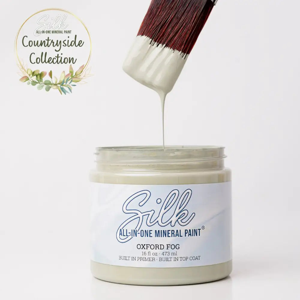 Jar of Silk all-in-one mineral paint with a brush dripping paint onto it, against a white background.