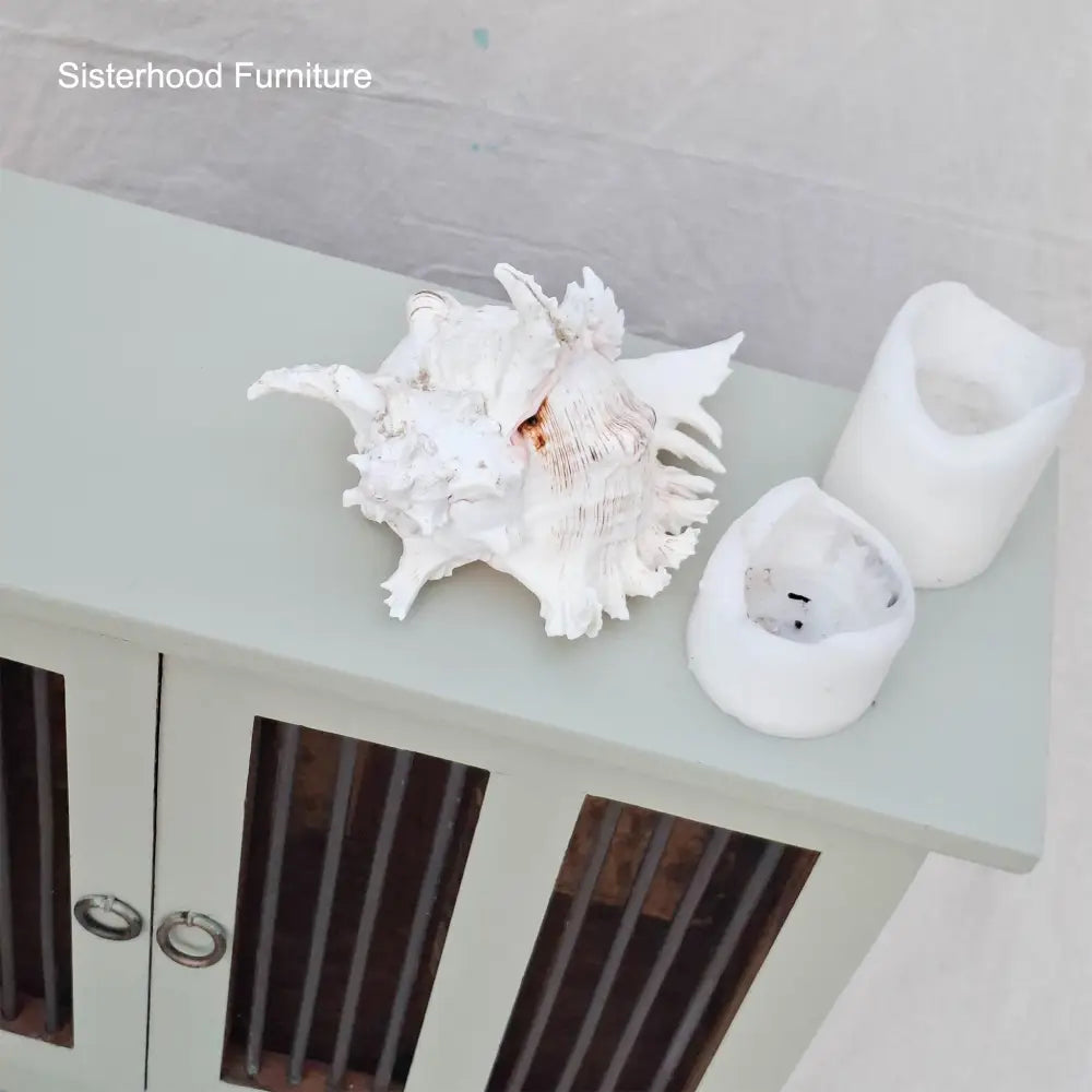 Decorative shell and candle holders on a light green surface with 'Sisterhood Furniture' branding.