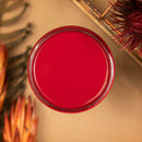 An arial view of an open container of Dixie Belle Paint Company's Fiery Sky All-In-One Silk Paint is on a light brown table with tropical red and orange plants.