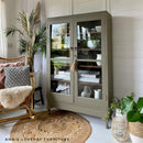 A bookcase with 2 large glass doors refurbished by Annie Loveday Furniture features Dixie Belle's Hampton Olive Silk All-In-One Mineral Paint.