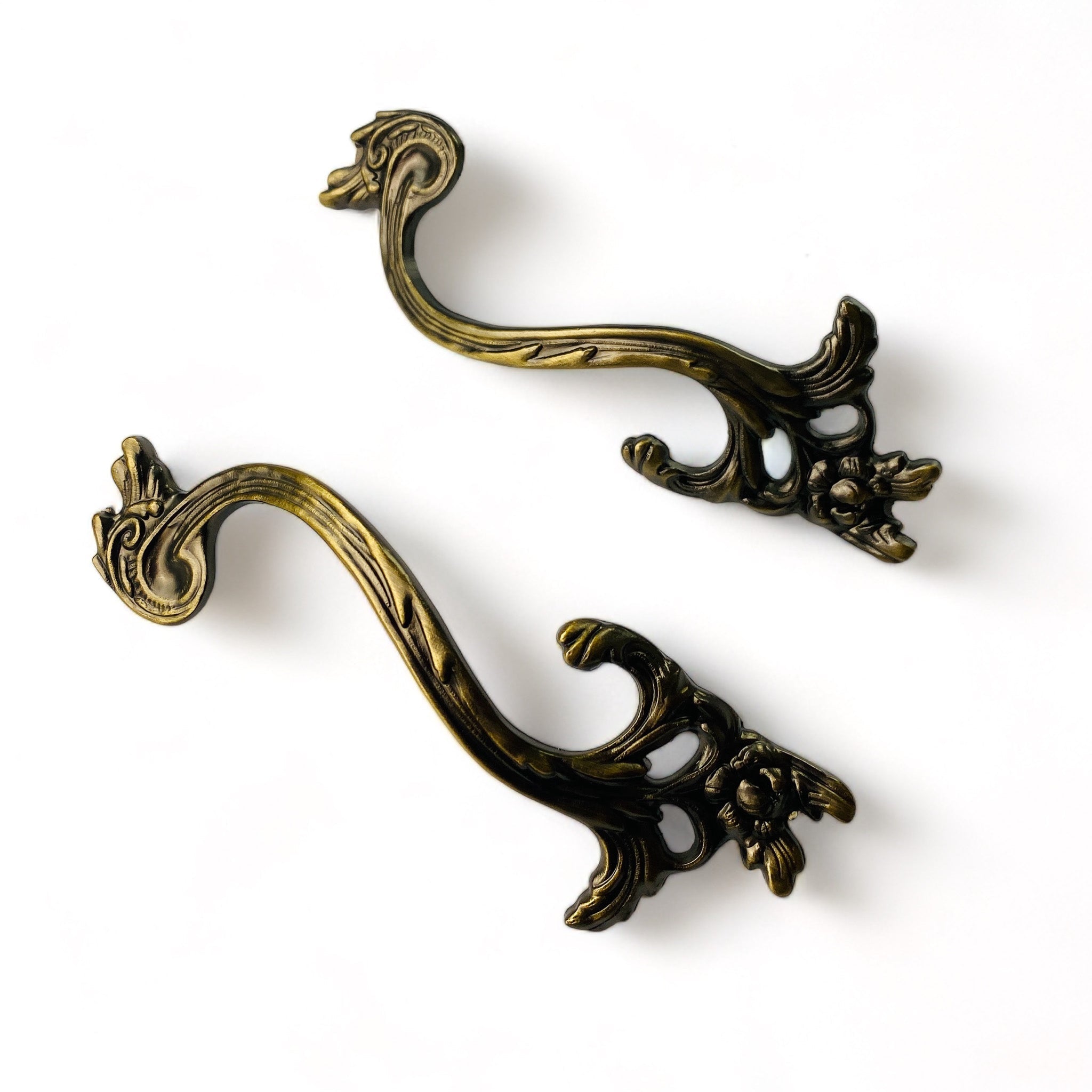 Two metal drawer pulls featuring subtle vines and leaves are against a white background.