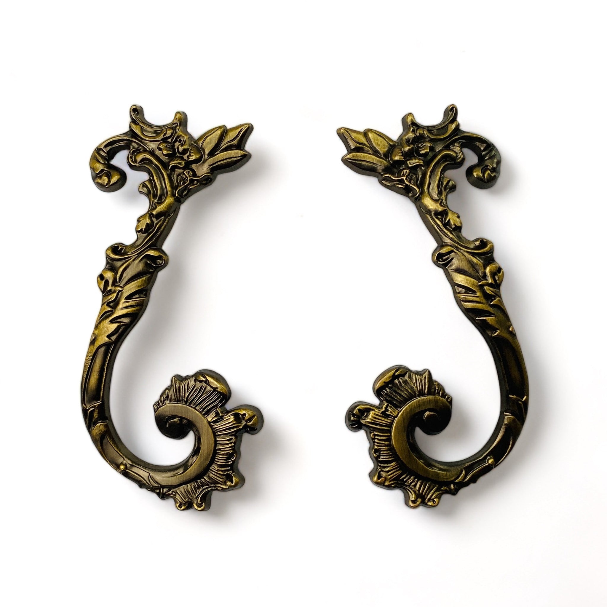 Two metal drawer pulls featuring swirling flourished and floral details are against a white background.