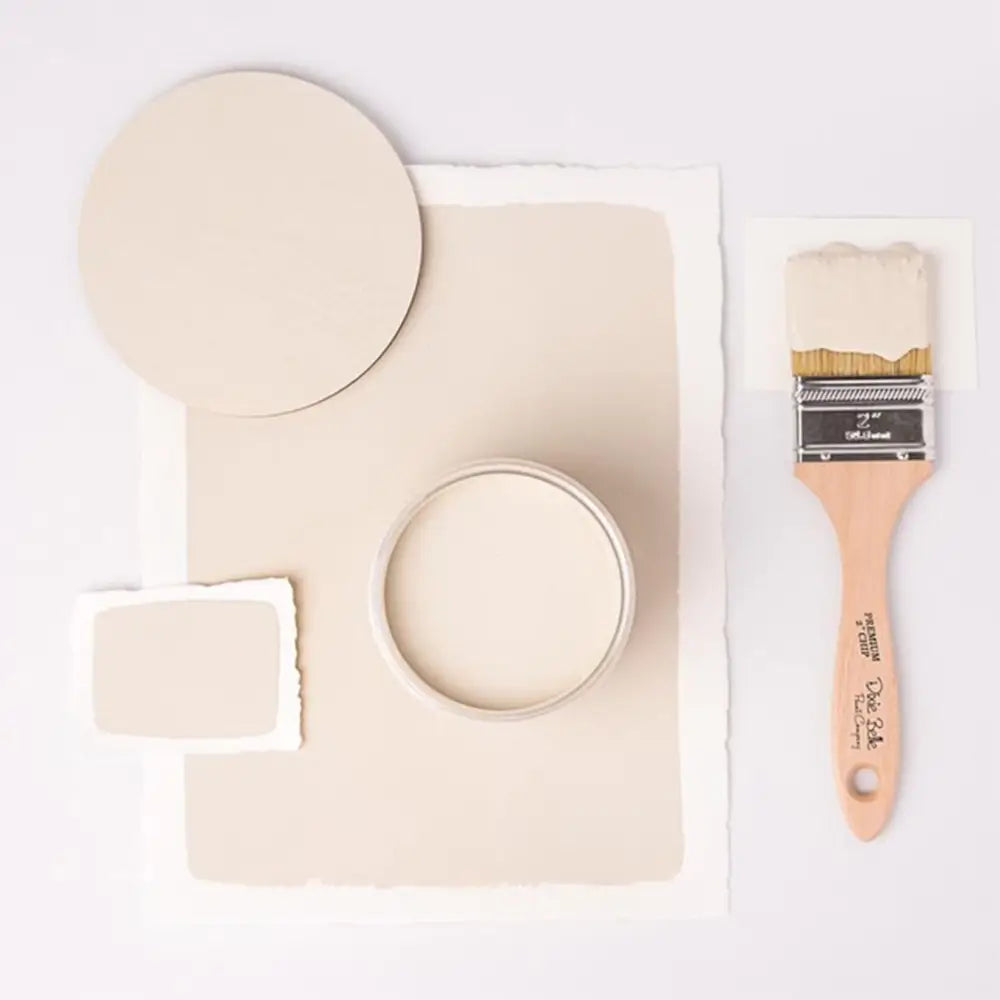 A paint brush, paper, and round wood samples of Dixie Belle's Ecru Chalk Mineral Paint are against a white background.