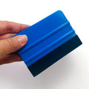 A hand is shown holding a 4 inch rectangular blue handled felt edge crafting squeegee against a white background.